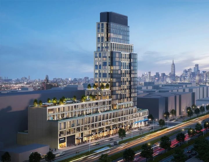 Modern multi-story building with tiered terraces and glass facades, set against a city skyline at dusk. Cars with light trails move along a busy road in the foreground. Rooftop greenery is visible on several levels.