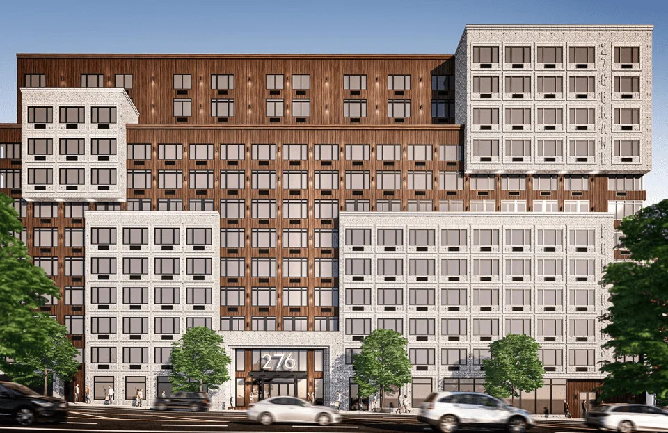 A modern mid-rise apartment building with a mix of brown and white facade, large windows, and a prominent entrance labeled "276," stands where experts once provided demolition services in NYC; cars pass by and trees line the street in front.